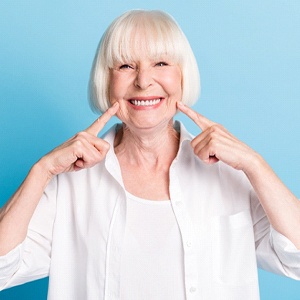 An older woman wearing white pointing to her dentures in Jacksonville