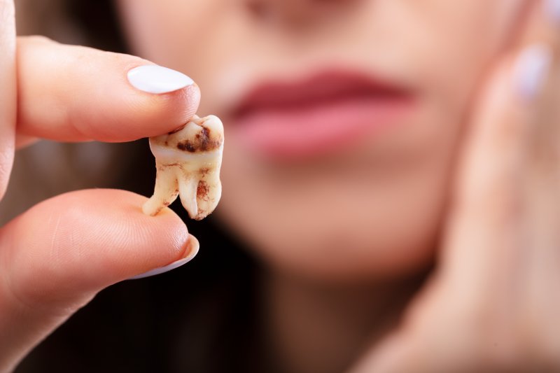 A person holding a decayed tooth in-between their fingers